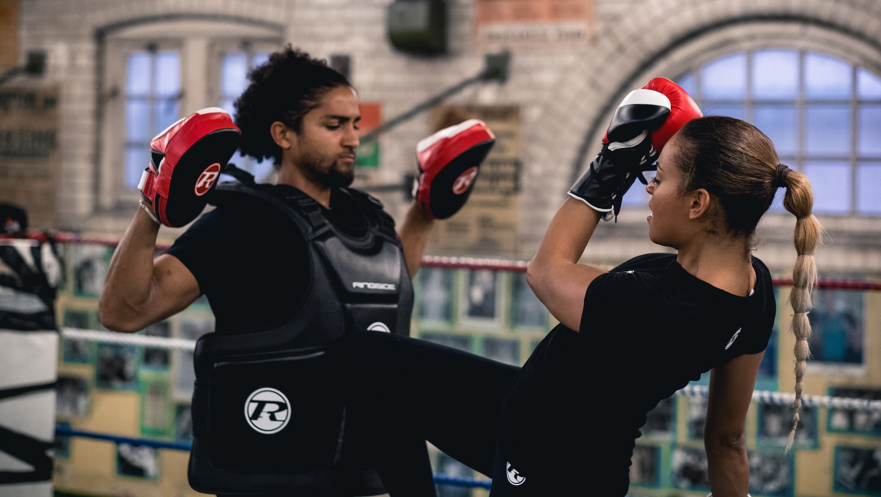 Coach wearing body protector and pads being kneed by kickboxer