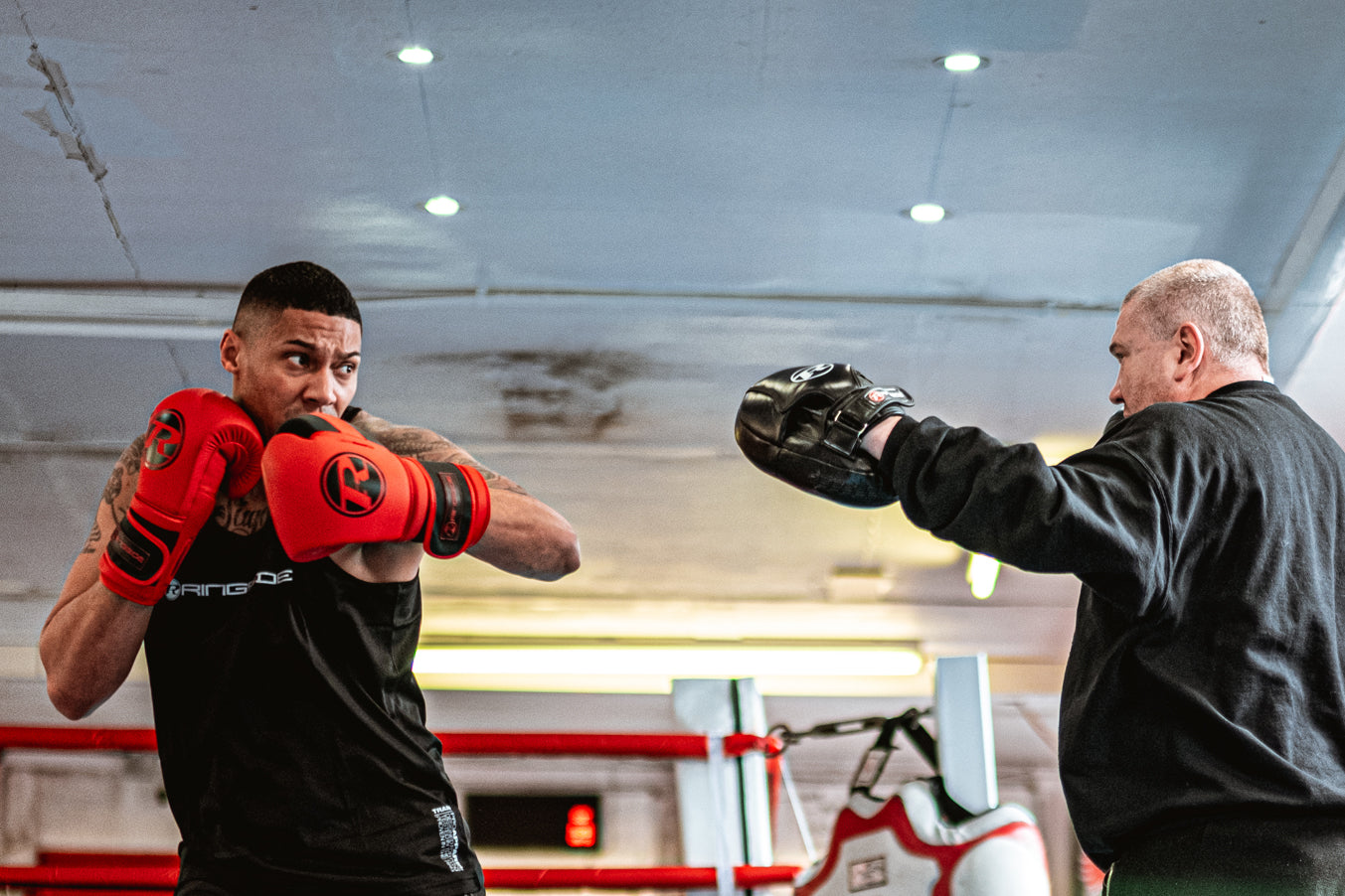 Boxer wearing red boxing gloves hitting pads which are being held by trainer